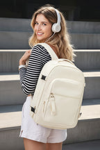 A woman wearing white over-ear headphones and a black-and-white striped long-sleeve top carries a cream-colored backpack with silver zippers, standing on outdoor concrete steps.